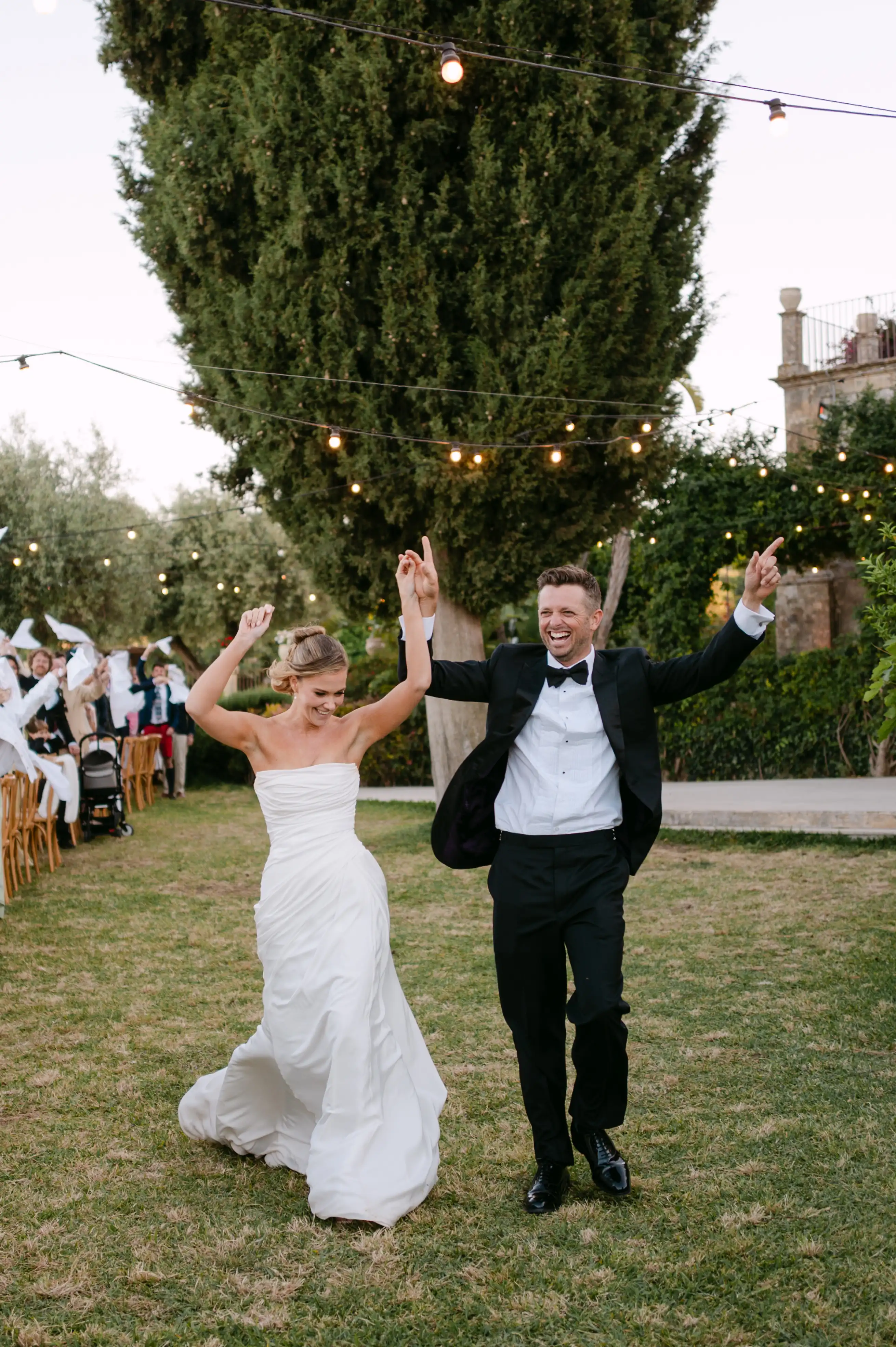 Bride and groom joyfully entering the outdoor wedding reception under string lights at a luxury Sicilian villa.